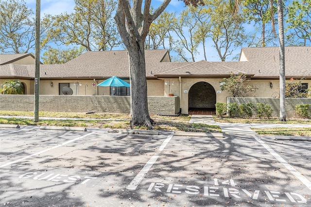 view of front of home with stucco siding, uncovered parking, a shingled roof, and fence