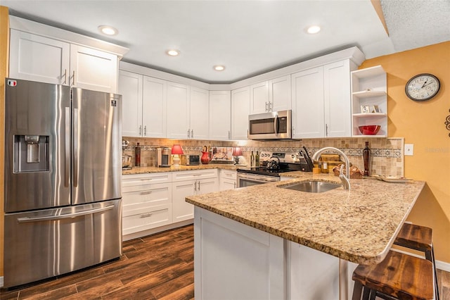 kitchen with a sink, appliances with stainless steel finishes, a peninsula, white cabinets, and open shelves