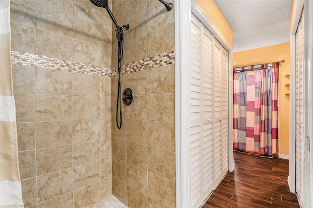 full bathroom featuring wood finished floors, a tile shower, and a textured ceiling