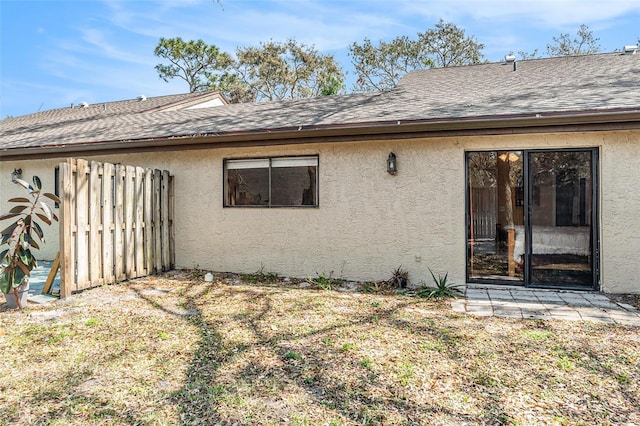 back of property featuring fence, roof with shingles, and stucco siding