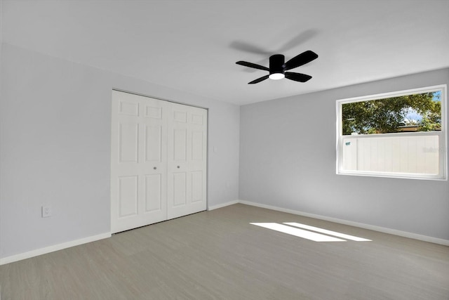 unfurnished bedroom featuring ceiling fan, a closet, baseboards, and wood finished floors