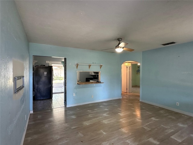 unfurnished living room with arched walkways, visible vents, baseboards, and wood finished floors