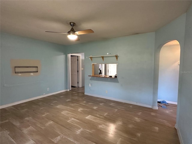 empty room with ceiling fan, baseboards, arched walkways, and wood finished floors