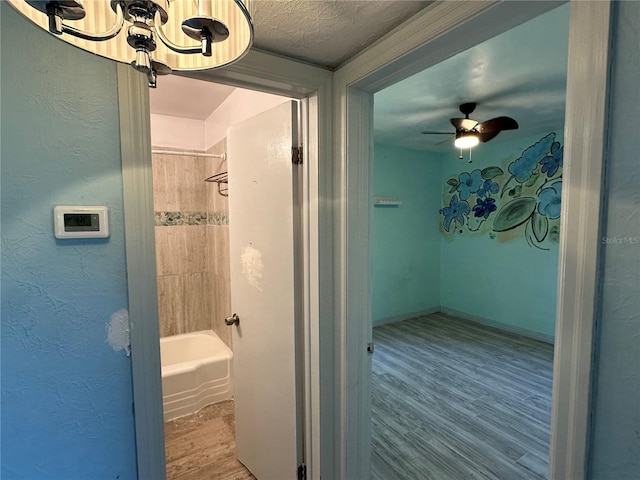 bathroom featuring shower / bath combination, wood finished floors, a textured wall, and a textured ceiling