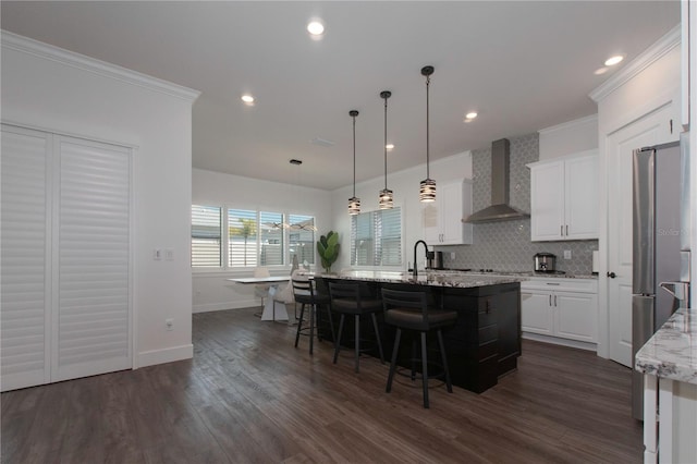 kitchen featuring a center island with sink, wall chimney exhaust hood, white cabinets, and ornamental molding