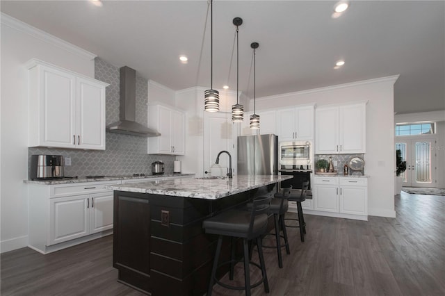 kitchen featuring an island with sink, a sink, appliances with stainless steel finishes, wall chimney exhaust hood, and crown molding