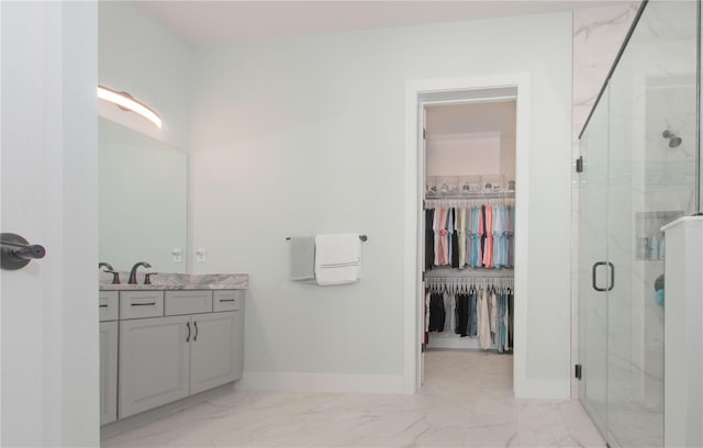 full bathroom featuring marble finish floor, vanity, a shower stall, baseboards, and a spacious closet