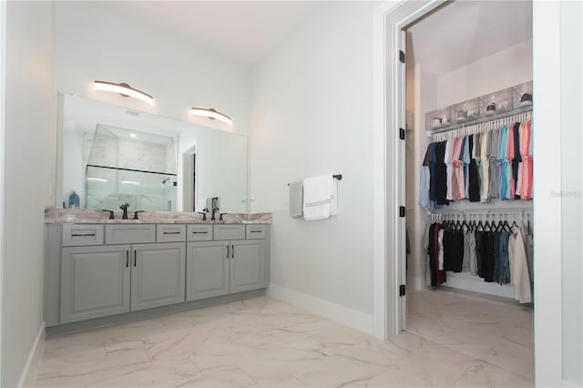 full bathroom featuring a marble finish shower, a walk in closet, baseboards, double vanity, and marble finish floor