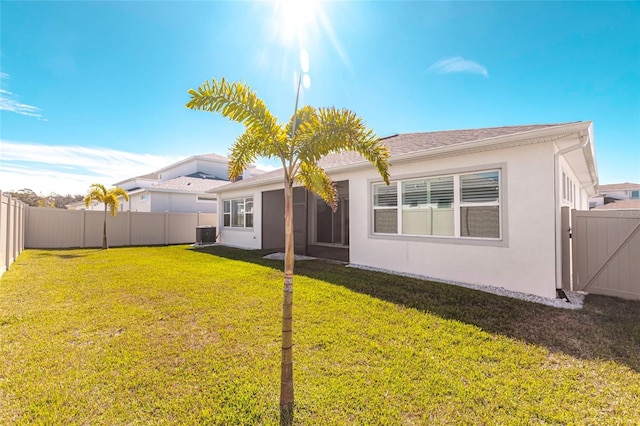 back of property featuring central AC, a lawn, a fenced backyard, and stucco siding