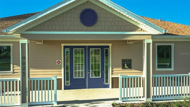 view of exterior entry with a porch and roof with shingles