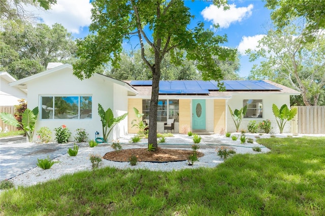 ranch-style home with stucco siding, solar panels, a front yard, and fence