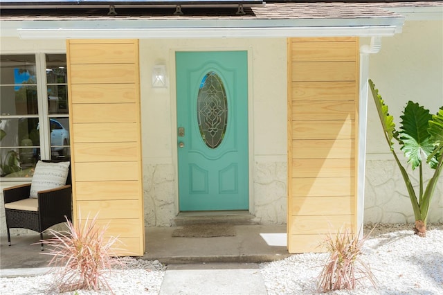 view of exterior entry with stucco siding and a shingled roof