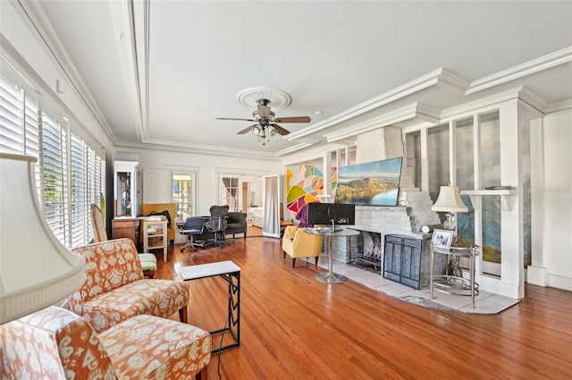 living area featuring a brick fireplace, crown molding, a ceiling fan, and wood finished floors