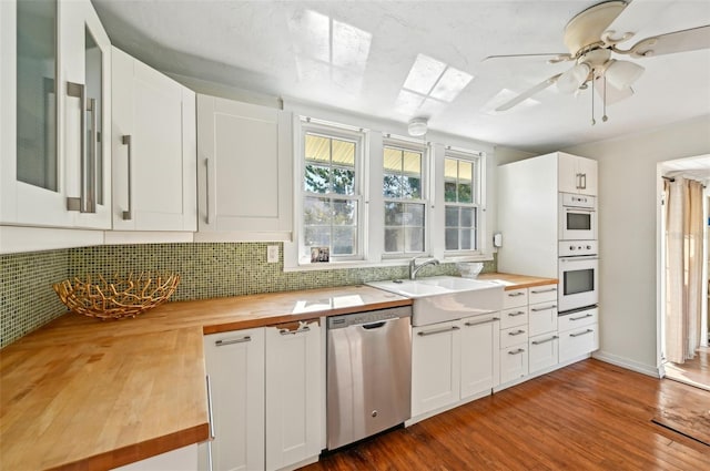 kitchen featuring white cabinetry, dark wood finished floors, a sink, stainless steel dishwasher, and butcher block counters