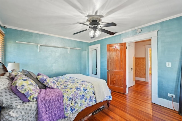 bedroom featuring a ceiling fan, baseboards, wood finished floors, ornamental molding, and a closet