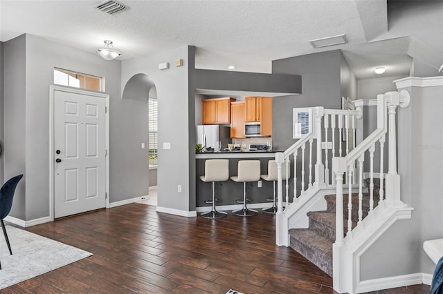 foyer entrance with hardwood / wood-style floors, visible vents, baseboards, arched walkways, and a textured ceiling