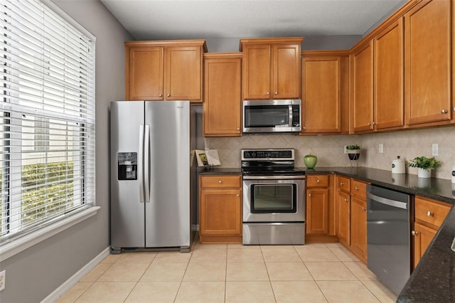 kitchen featuring light tile patterned floors, stainless steel appliances, brown cabinetry, and tasteful backsplash