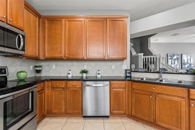 kitchen with light tile patterned flooring, brown cabinets, appliances with stainless steel finishes, and a sink