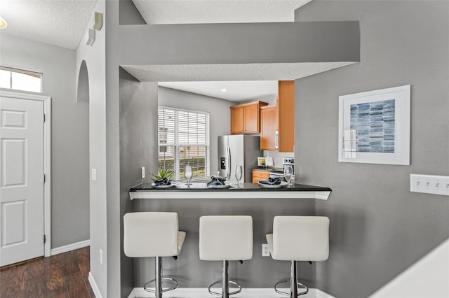 kitchen featuring dark countertops, baseboards, a breakfast bar, stainless steel appliances, and dark wood-style flooring