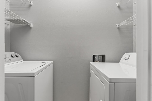 clothes washing area with laundry area, separate washer and dryer, and a textured wall