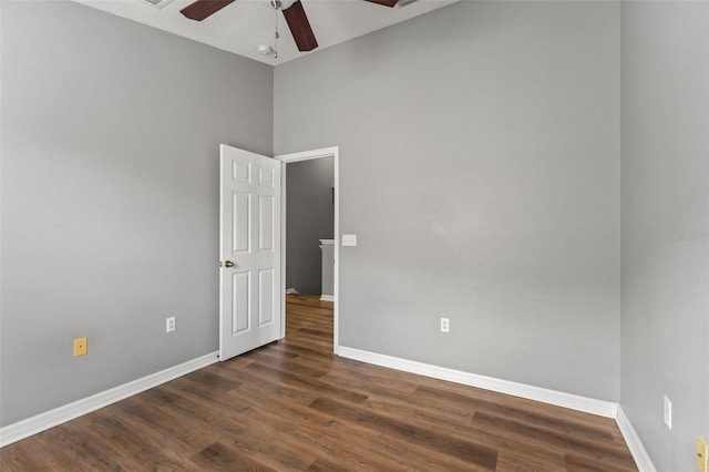 unfurnished room featuring baseboards, dark wood-style floors, and a ceiling fan