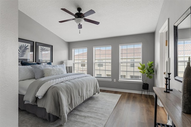 bedroom with lofted ceiling, a textured ceiling, wood finished floors, baseboards, and ceiling fan