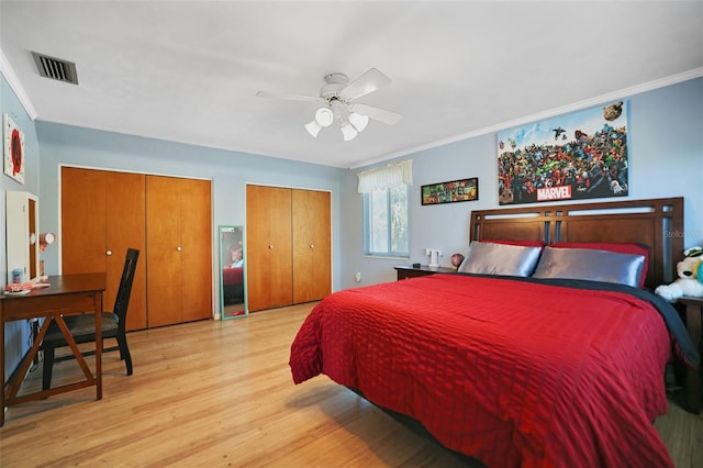 bedroom with visible vents, ceiling fan, multiple closets, crown molding, and light wood-type flooring