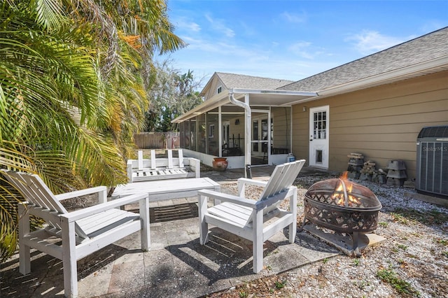 view of patio featuring central air condition unit, a fire pit, fence, and a sunroom