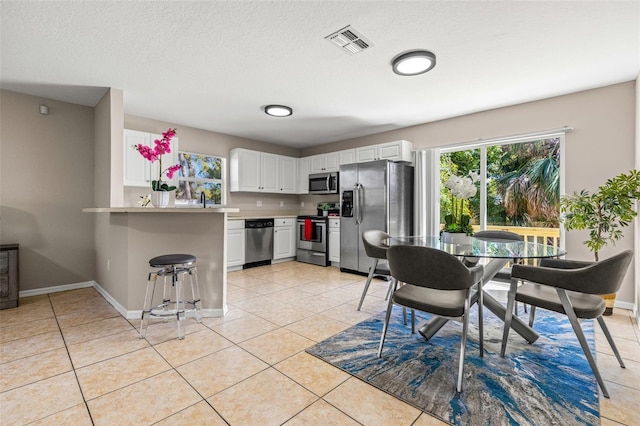 kitchen featuring light tile patterned floors, visible vents, a peninsula, stainless steel appliances, and white cabinets