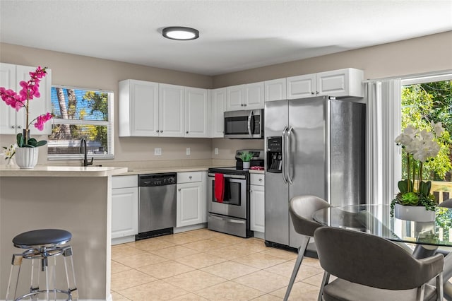 kitchen featuring a sink, stainless steel appliances, white cabinets, light tile patterned flooring, and light countertops