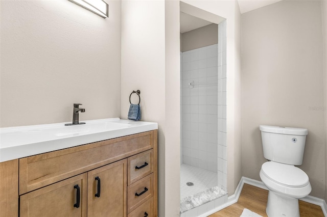 bathroom featuring vanity, wood finished floors, baseboards, a tile shower, and toilet