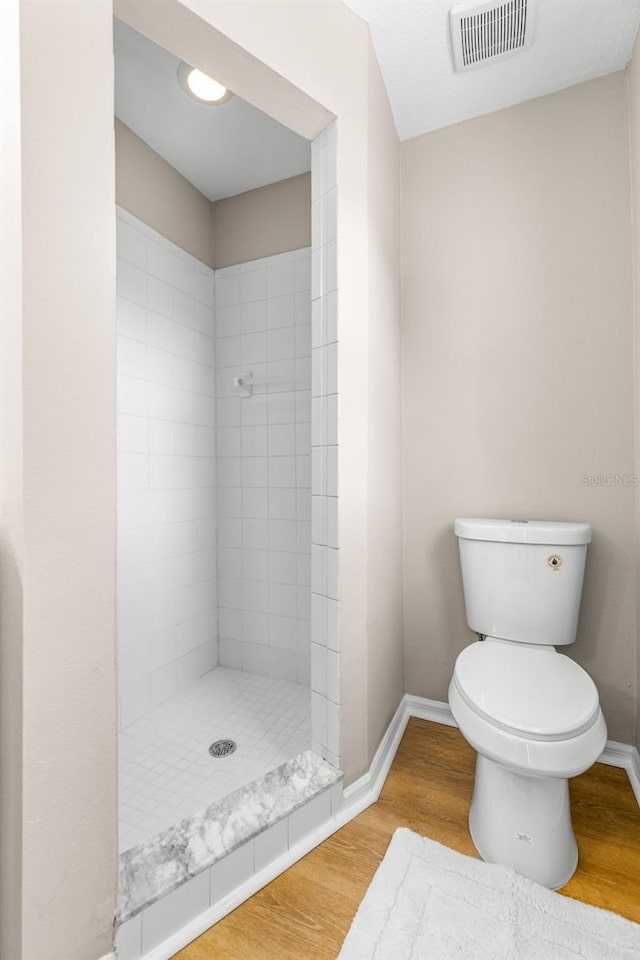 bathroom with visible vents, toilet, wood finished floors, baseboards, and tiled shower