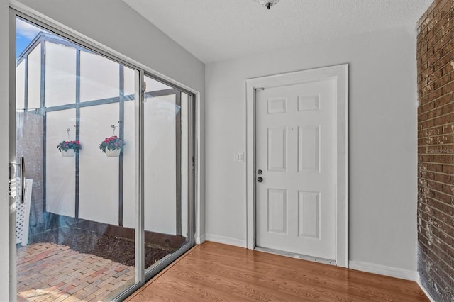 interior space with baseboards, a textured ceiling, wood finished floors, and brick wall