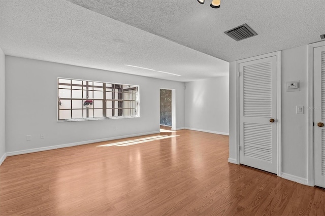 empty room with visible vents, baseboards, a textured ceiling, and wood finished floors