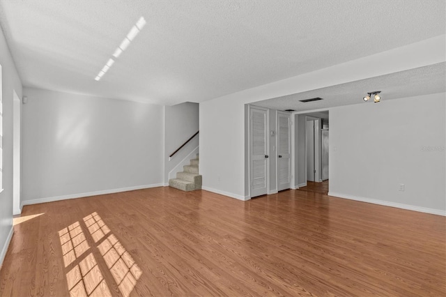 empty room with visible vents, baseboards, light wood-style flooring, stairs, and a textured ceiling