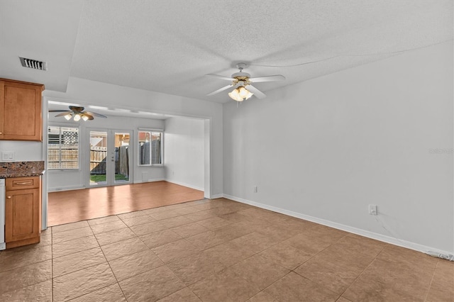 unfurnished living room featuring baseboards, a ceiling fan, visible vents, and a textured ceiling