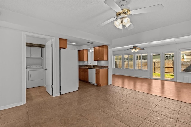 kitchen with dark countertops, open floor plan, brown cabinets, white appliances, and washer / clothes dryer