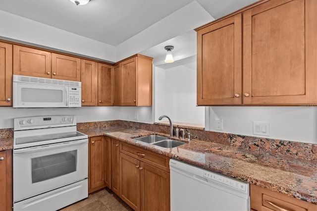 kitchen with white appliances, dark stone countertops, a sink, tile patterned flooring, and brown cabinets