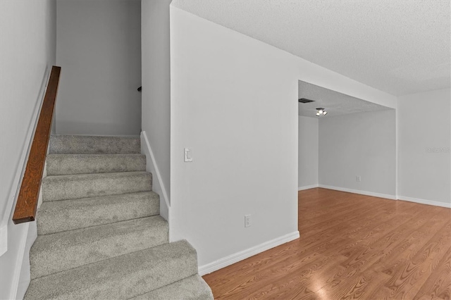 staircase featuring visible vents, baseboards, a textured ceiling, and wood finished floors