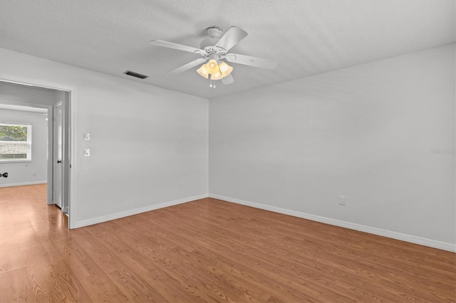 spare room with light wood-type flooring, visible vents, a textured ceiling, baseboards, and ceiling fan