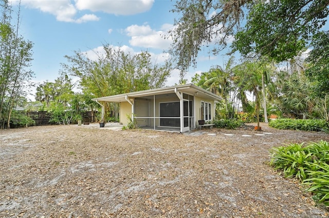 rear view of property with stucco siding, a sunroom, and fence