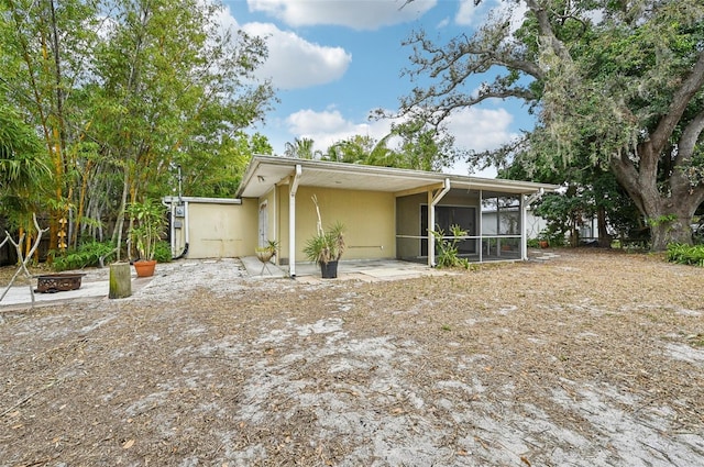 rear view of property with stucco siding, an outdoor fire pit, and a sunroom