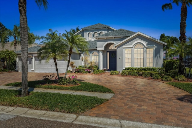 mediterranean / spanish house featuring stucco siding, an attached garage, and curved driveway