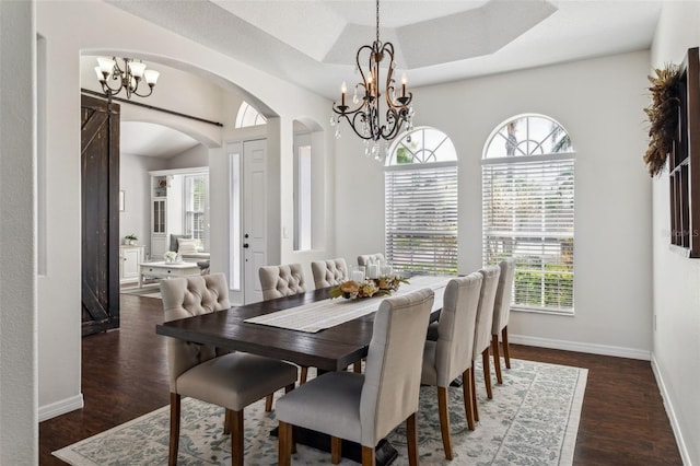 dining area with a tray ceiling, baseboards, arched walkways, and wood finished floors