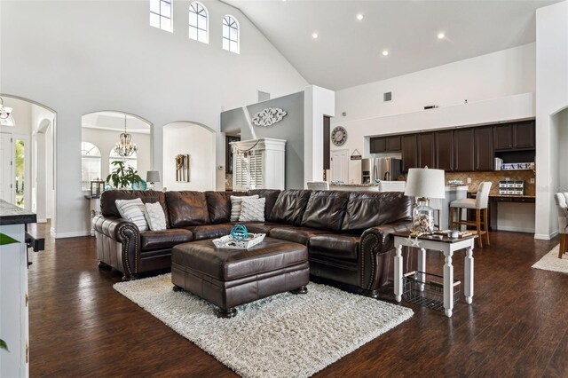 living room with arched walkways, a high ceiling, an inviting chandelier, and dark wood-style floors