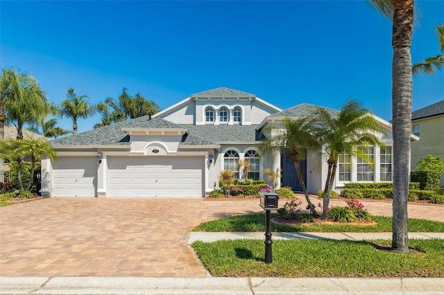 mediterranean / spanish-style home featuring decorative driveway, a garage, roof with shingles, and stucco siding