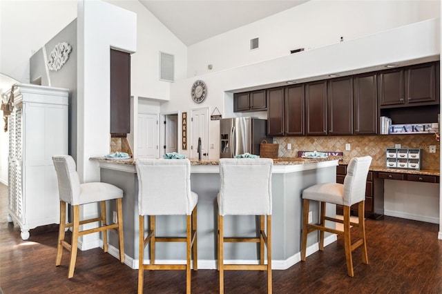 kitchen featuring visible vents, backsplash, stainless steel fridge with ice dispenser, dark brown cabinets, and dark wood-style flooring