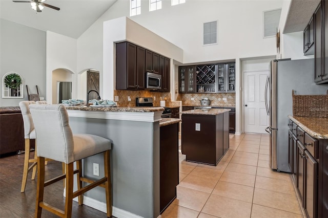 kitchen featuring visible vents, high vaulted ceiling, arched walkways, stainless steel appliances, and glass insert cabinets