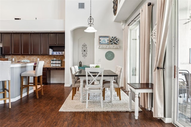 dining space with visible vents, baseboards, dark wood-type flooring, and a high ceiling