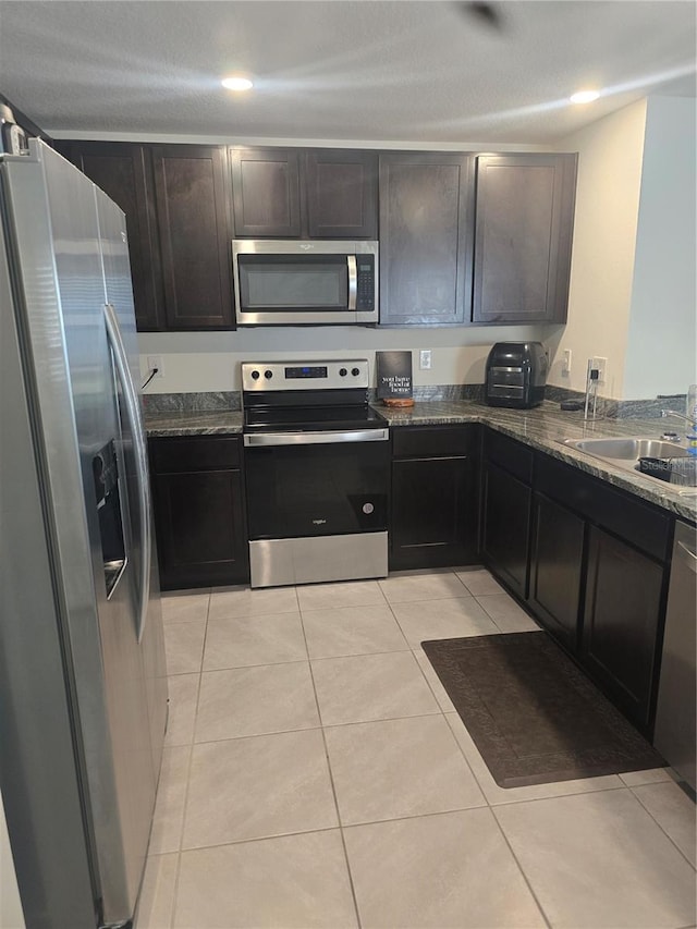 kitchen with light tile patterned flooring, appliances with stainless steel finishes, dark stone counters, and a sink